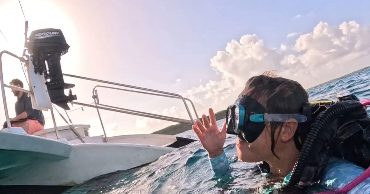 A scuba diver at the surface beside the dive boat at sunset
