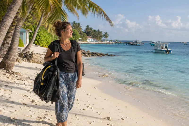 Solo woman diver walking on a local island beach in the Maldives