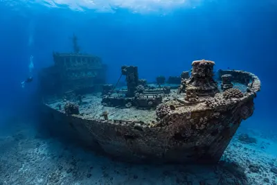 A large underwater shipwreck on a sandy seabed in clear blue water